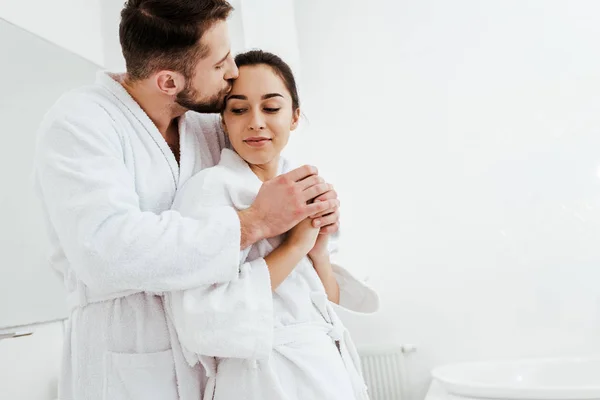 Cheerful man kissing happy girlfriend while holding hands in bathroom — Stock Photo