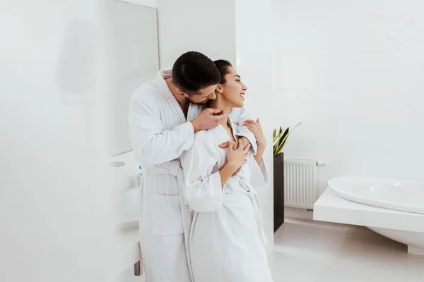 Foco seletivo do homem barbudo tocando o pescoço da namorada feliz enquanto está em pé no banheiro — Fotografia de Stock
