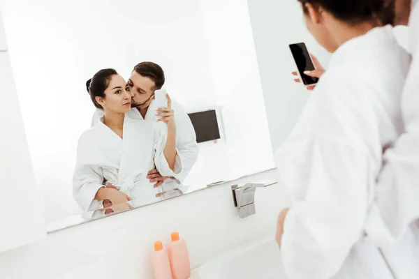 Enfoque selectivo de la mujer tomando fotos mientras su novio besa mejilla en el baño - foto de stock