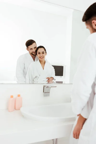 Selective focus of bearded man looking at mirror with happy brunette woman — Stock Photo