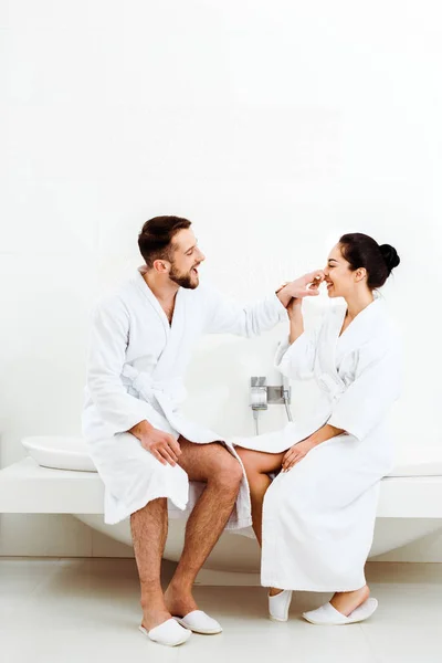 Happy bearded man sitting touching nose of cheerful woman in bathrobe — Stock Photo