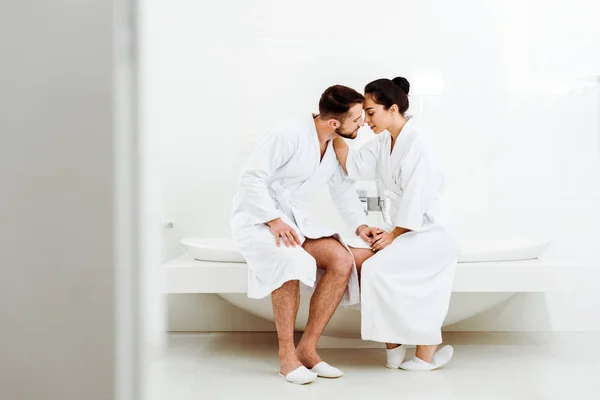 Selective focus of bearded man sitting and holding hands with attractive girl in bathrobe — Stock Photo