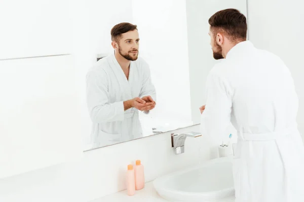Selective focus of handsome bearded man looking at mirror in bathroom — Stock Photo
