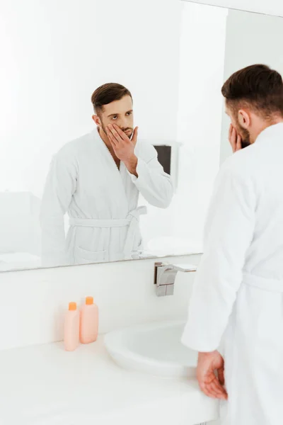 Selective focus of upset bearded man looking at mirror in bathroom — Stock Photo