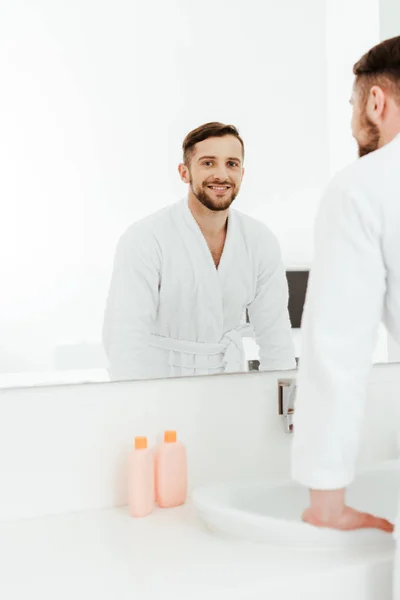 Selektiver Fokus eines glücklichen bärtigen Mannes, der neben Spiegel im Badezimmer steht — Stockfoto