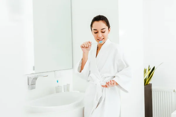 Mulher morena segurando escova de dentes com pasta de dentes e olhando para a mão — Fotografia de Stock