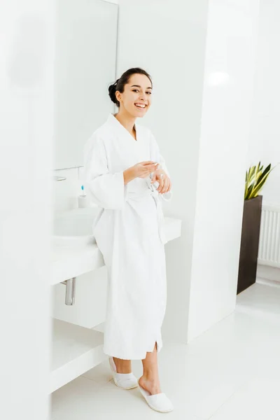 Fröhliche und attraktive junge Frau, die im Badezimmer Handcreme aufträgt — Stockfoto