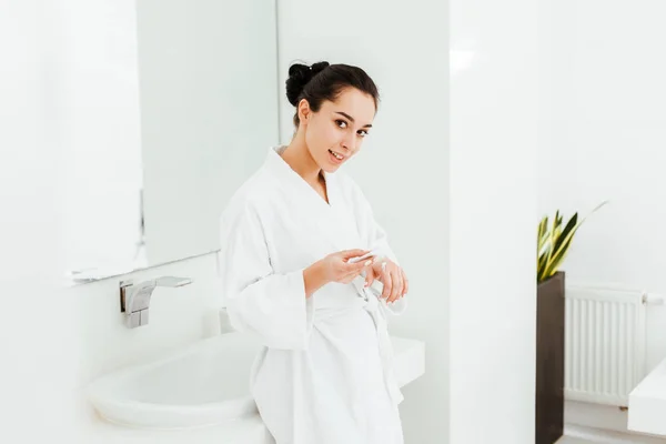 Счастливая и привлекательная женщина наносит крем для рук в ванной — стоковое фото