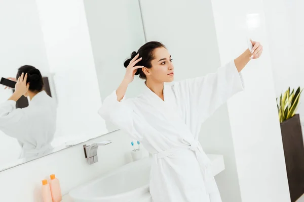 Селективный фокус привлекательной молодой женщины, делающей селфи в ванной комнате — стоковое фото