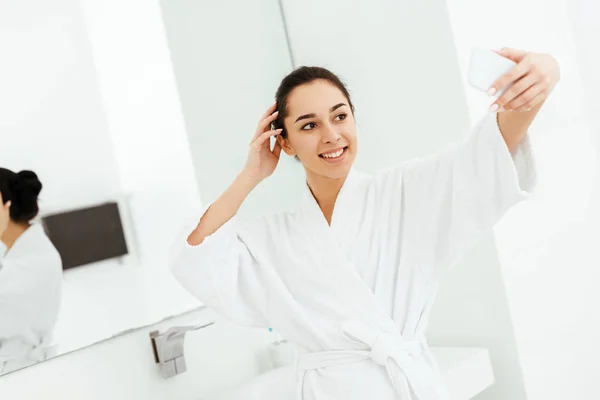 Селективный фокус счастливой молодой женщины, делающей селфи в ванной комнате — стоковое фото