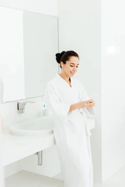 Happy brunette woman listening musing in earphones in bathroom — Stock Photo