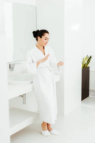 Happy brunette girl listening musing in earphones in bathroom — Stock Photo