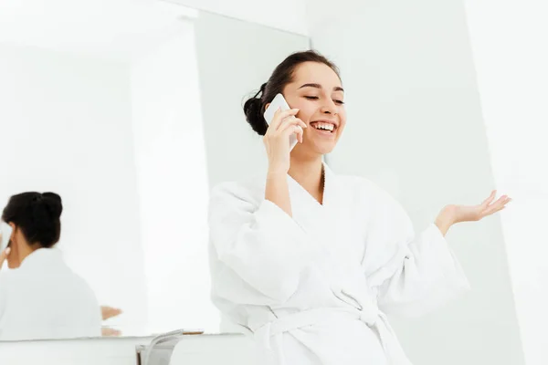 Низкий угол зрения счастливой молодой женщины жестикулируя во время разговора на смартфоне в ванной комнате — стоковое фото