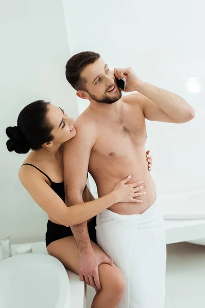 Brunette woman in underwear looking at happy boyfriend talking on smartphone — Stock Photo