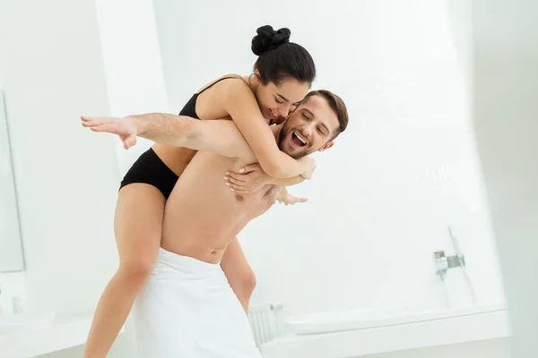 Щасливий без сорочки чоловік скарбничка посміхається дівчина в чорній нижній білизні у ванній — стокове фото