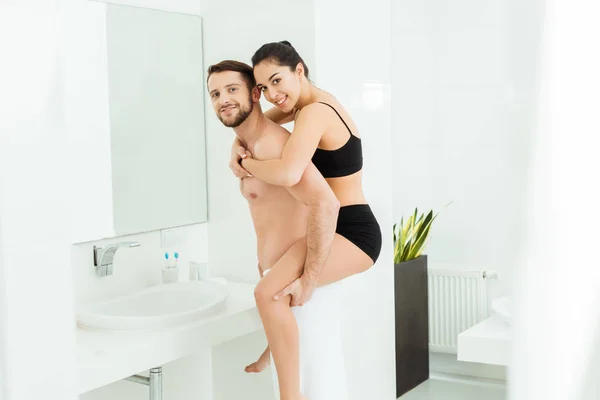 Alegre sin camisa hombre piggybacking morena novia en negro ropa interior - foto de stock