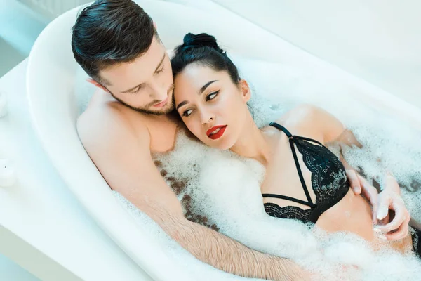 Overhead view of handsome man lying in bathtub with attractive brunette woman in lace bra — Stock Photo