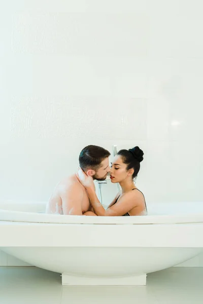 Morena mujer abrazando guapo sin camisa hombre en bañera - foto de stock