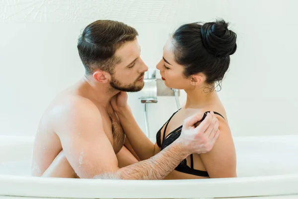 Bärtige Mann ohne Hemd suchen und berühren sexy brünette Frau in schwarzen BH — Stockfoto