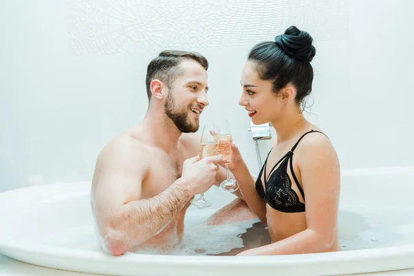 Gai homme torse nu cliquetis champagne verre avec fille heureuse dans la baignoire — Photo de stock