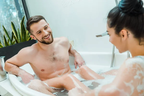 Foco seletivo do homem alegre olhando para a mulher morena na banheira — Fotografia de Stock