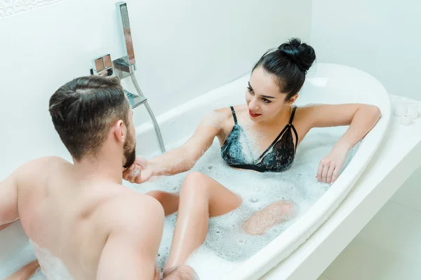 Blick von oben auf fröhliche Frau, die Gesicht eines hemdlosen Mannes in Badewanne berührt — Stockfoto