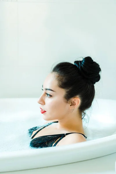 Attractive brunette woman lying in bathtub with bath foam — Stock Photo