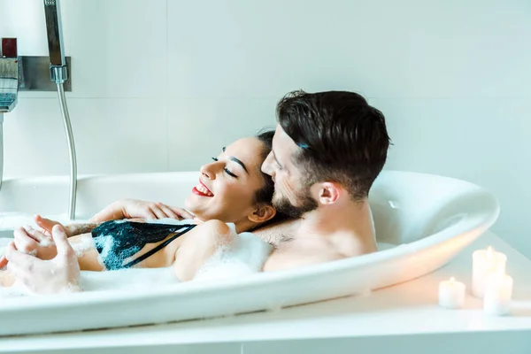 Feliz morena joven mujer acostada con barbudo hombre en bañera - foto de stock
