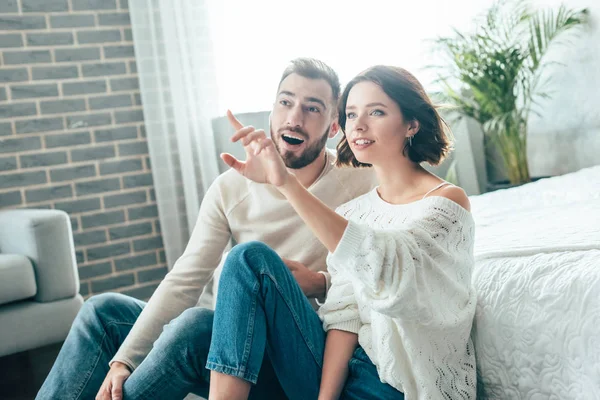 Atractiva mujer morena señalando con el dedo mientras está sentado con un hombre guapo en casa - foto de stock