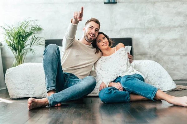 Glücklicher Mann umarmt attraktive Frau, während er mit dem Finger zeigt und Film zu Hause anschaut — Stockfoto