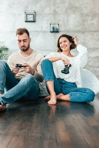 Tiefansicht einer glücklichen Frau, die einen aufgebrachten Mann mit Steuerknüppel zu Hause betrachtet — Stockfoto