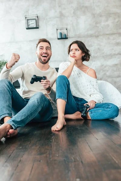 Low angle view of upset woman looking at happy man gesturing while playing video game — Stock Photo