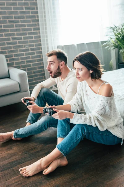 Sorprendido hombre y atractiva mujer jugando videojuego en casa - foto de stock