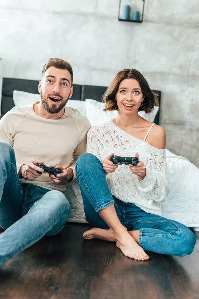 Homem surpreso e mulher alegre jogando videogame em casa — Fotografia de Stock