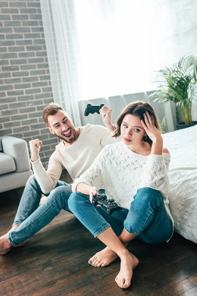 Glücklicher Mann schaut aufgebrachtes Mädchen an, das mit Joystick auf dem Boden sitzt — Stockfoto