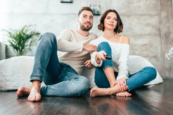 Low angle view of happy man sitting on floor near attractive woman with remote controller — Stock Photo