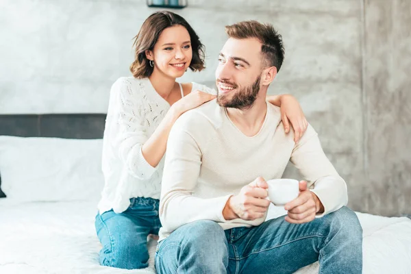 Cheerful woman hugging happy man holding cup with coffee — Stock Photo