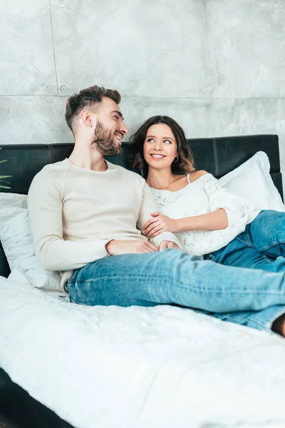 Selective focus of cheerful man lying on bed and looking at attractive woman at home — Stock Photo