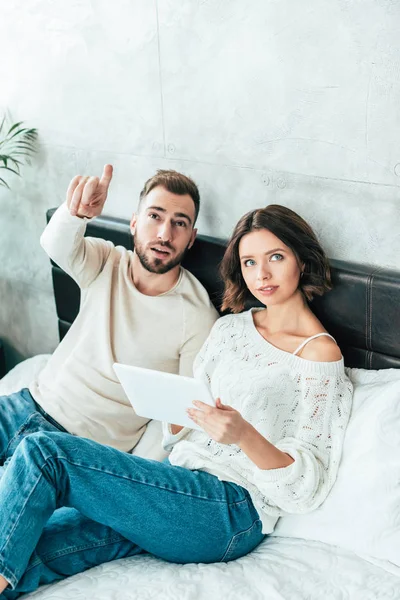 Hombre guapo señalando con el dedo cerca de mujer hermosa con tableta digital - foto de stock