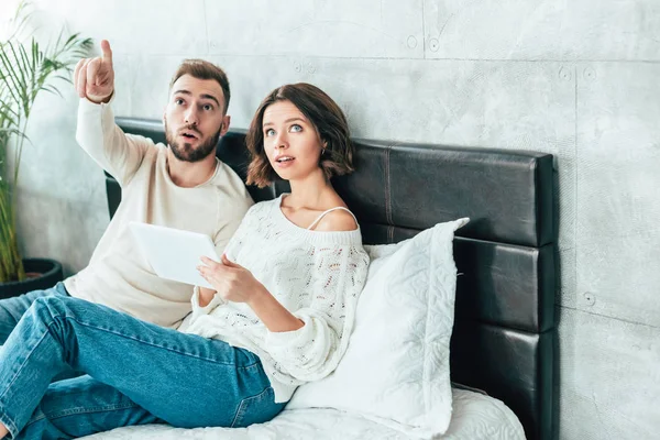 Homem bonito apontando com o dedo perto mulher surpreso com tablet digital — Fotografia de Stock