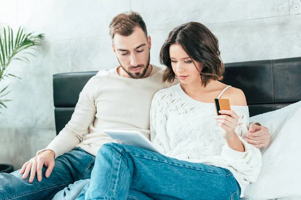 Schöner Mann schaut auf digitales Tablet neben attraktiver Frau mit Kreditkarte — Stockfoto