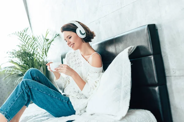 Glückliche brünette Frau mit Kopfhörer, Tasse in der Hand und Musik hören — Stockfoto