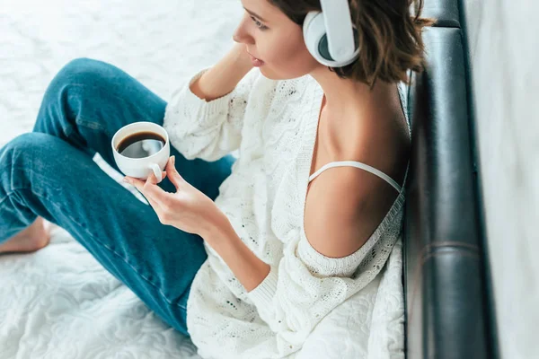 Vista aerea della donna bruna in cuffia che tiene la tazza e ascolta la musica — Foto stock