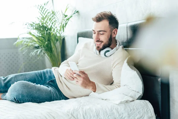 Foyer sélectif de l'homme barbu heureux dans les écouteurs en utilisant smartphone dans les écouteurs — Photo de stock