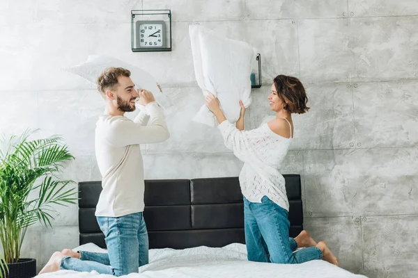 Homem feliz ter travesseiro luta com mulher atraente na cama — Fotografia de Stock