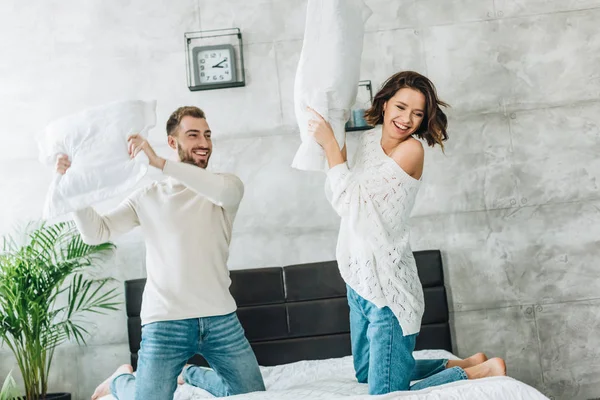 Mulher alegre ter travesseiro luta com homem feliz no quarto — Fotografia de Stock