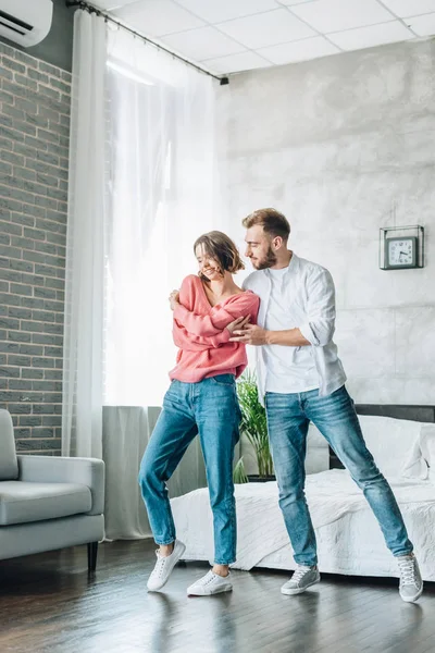 Mulher feliz dançando com homem barbudo bonito no quarto — Fotografia de Stock