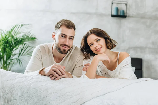 Cheerful man and happy woman looking at camera in bedroom — Stock Photo
