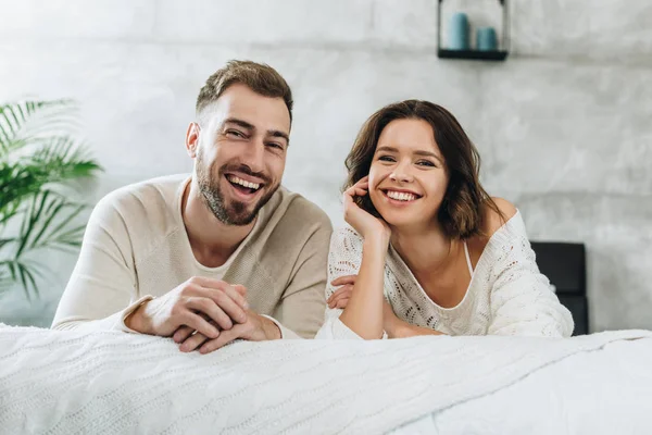 Feliz hombre y sonriente morena mujer mirando a la cámara en el dormitorio - foto de stock