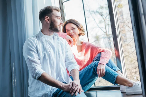 Vista de ángulo bajo de la mujer atractiva sentada cerca de la ventana con el hombre guapo en casa - foto de stock